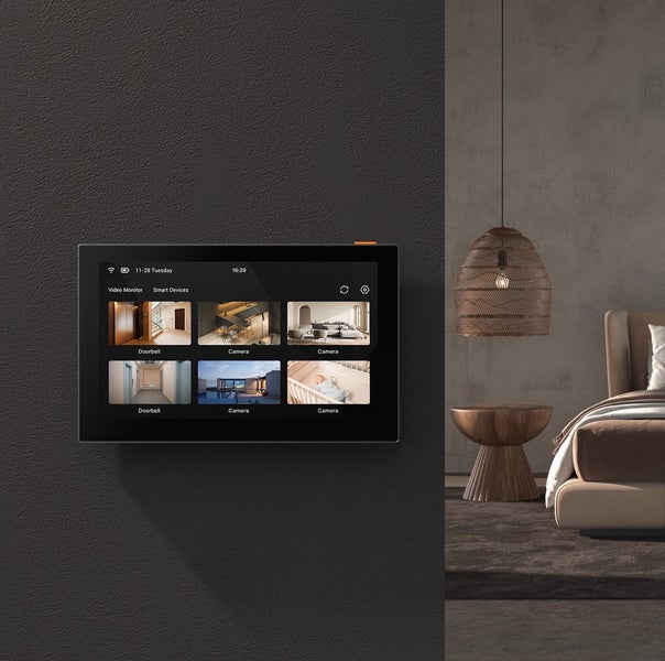 Smart Home Bedienpanel an der Wand mit Videoüberwachung verschiedener Räume in einem modern eingerichteten Schlafzimmer.