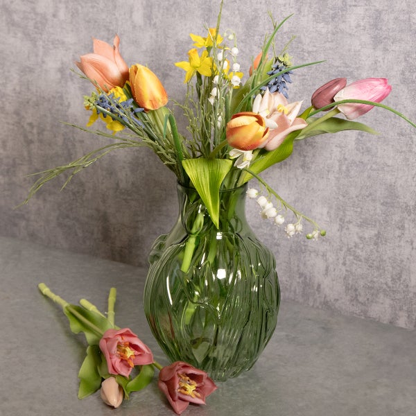 Künstlicher Blumenstrauß mit Tulpen, Narzissen und Maiglöckchen in einer grünen Glasvase mit Struktur, dekorativ arrangiert.