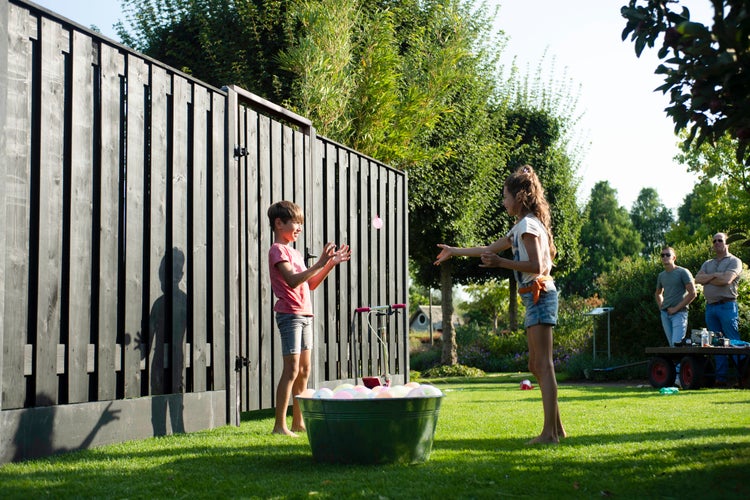 Szene im Garten mit Holzzaun, Kindern und einer Wanne voller Wasserbomben.