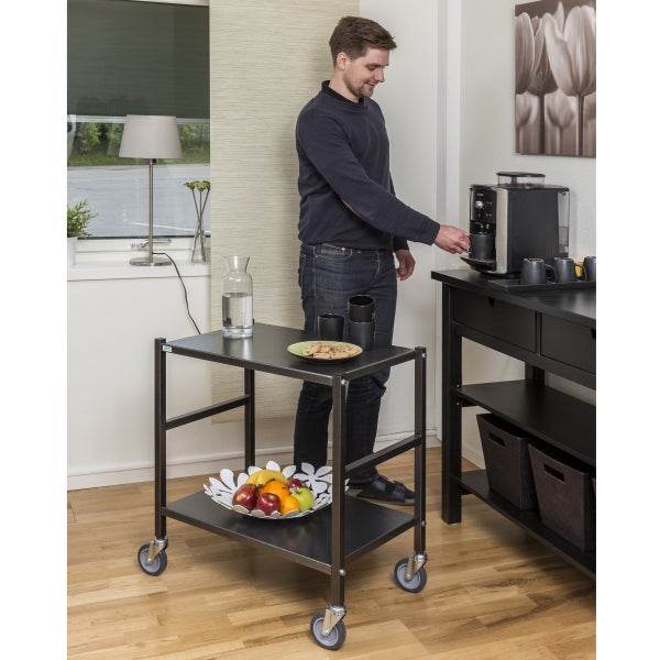 Szene mit einem Servierwagen, einem Mann, der Kaffee zubereitet, und einer Kaffeestation in einem hellen Raum.