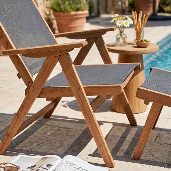 Gartenstuhl und Fußhocker aus Holz mit Textilbespannung auf einer Terrasse am Pool.