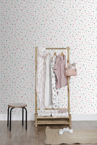 Helle, freundliche Szene mit Kleiderständer, Kinderkleidung und passenden Accessoires vor einer bunten Wand