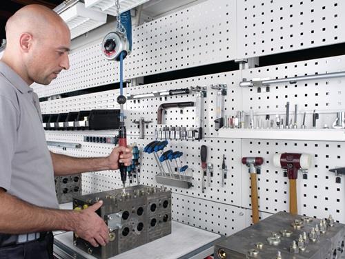 Werkstatt mit Werkzeugwand und Mechaniker bei der Arbeit an einem Metallblock