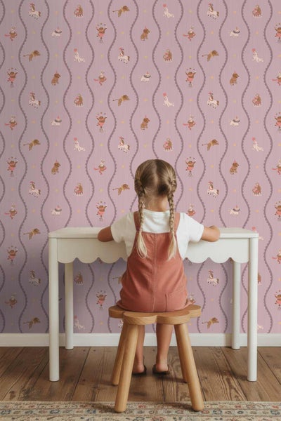 Kind am weißen Schreibtisch vor einer Mustertapete mit Zirkusmotiven wie Affen, Löwen und Pferden in einem Kinderzimmer.