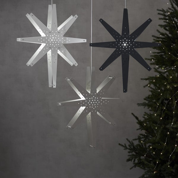 Drei dekorative Sterne, aus Metall mit Beleuchtung, hängen vor einer Wand und einem Weihnachtsbaum.
