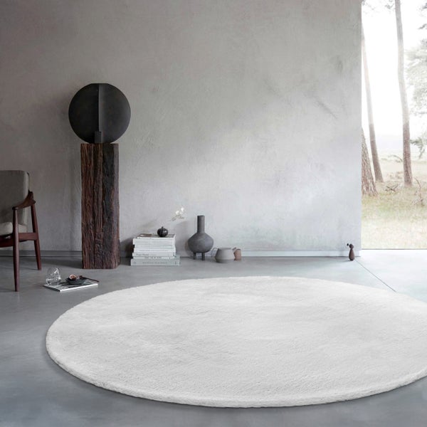 Großer runder weicher Teppich in einem modernen Wohnzimmer mit Betonboden und minimalistischer Dekoration.