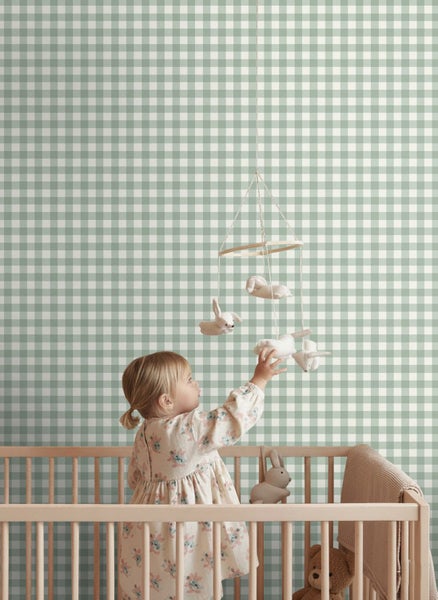 Vlies-Tapete mit grünem Karo-Muster im Kinderzimmer hinter einem Gitterbett mit einem Baby.