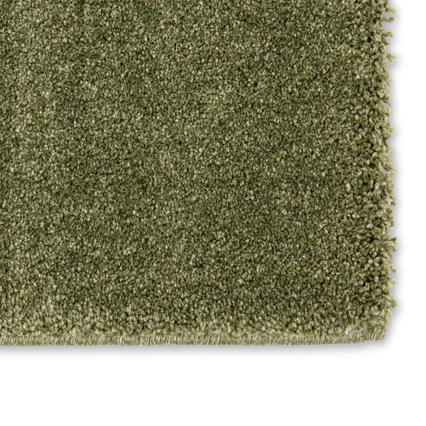Nahaufnahme eines grünen Hochflor-Teppichs mit sichtbarer Textur und Kante.