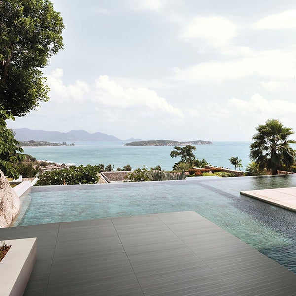 Terrasse mit modernen dunklen Fliesen am Infinity Pool mit Blick auf das Meer und eine tropische Bucht.