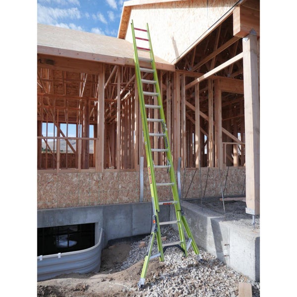 Lange Mehrzweckleiter aus Aluminium lehnt an einem Holzrahmen-Haus auf einer Baustelle.