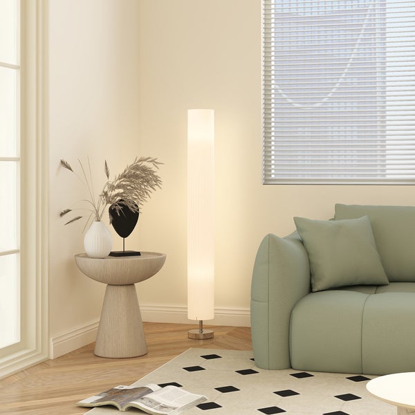 Moderne zylindrische Stehleuchte in einem hellen Wohnzimmer neben einem grünen Sofa und einem runden Beistelltisch.