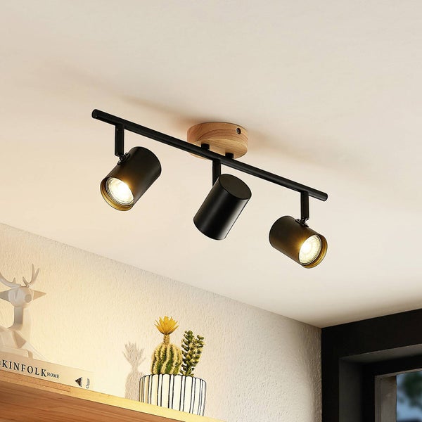 Moderne Deckenleuchte mit drei verstellbaren Spots aus Metall und einer Holzbasis, montiert in einem hellen Raum über einem Regal.