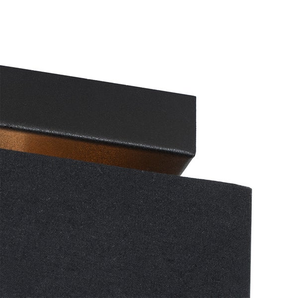 Detailansicht einer Leuchte mit schwarzem Textilschirm und schwarzem Metallrahmen mit goldfarbener Innenseite.