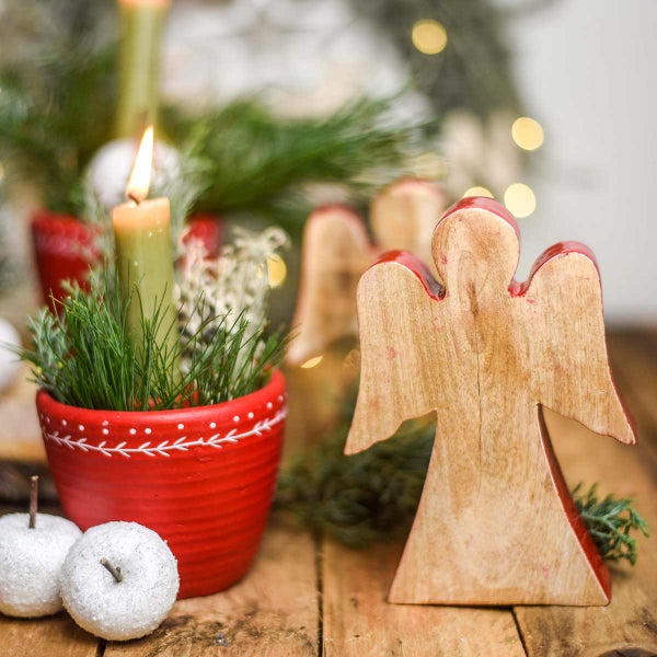 Dekorative Weihnachtsszene mit Holzengel, bepflanztem Topf und Kerze auf einem Holztisch