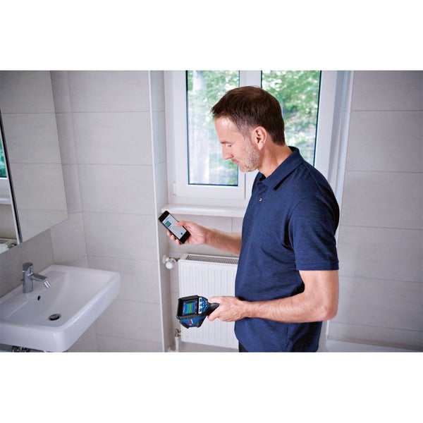 Mann mit Thermodetektor und Smartphone im Badezimmer