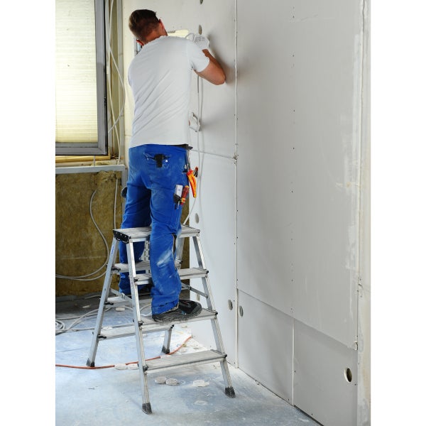 Handwerker auf einer Trittleiter bei der Installation von Elektrik in einem Raum mit Gipskartonplatten.