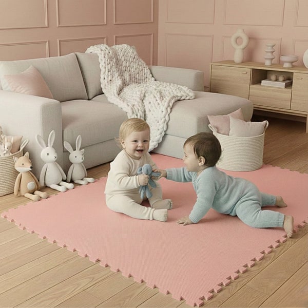 Zwei Babys spielen auf einer weichen, rosa Puzzlematte im Wohnzimmer. Die Schaumstoffmatte hat verzahnte Ränder. Heller Raum mit Parkettboden.