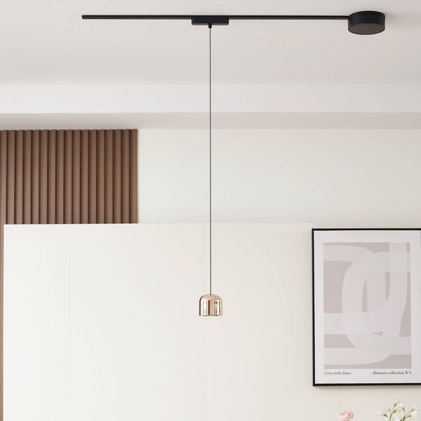 Moderne Schienensystem-Pendelleuchte mit kupferfarbenem Schirm an schwarzer Deckenschiene in hellem Raum mit Holzelementen.
