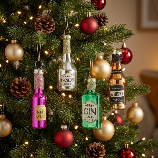 Weihnachtsbaumschmuck in Form von Getränkeflaschen wie Prosecco, Gin, Whisky und Rotwein hängend an einem geschmückten Tannenbaum.