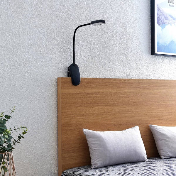 Schwarze LED-Klemmlampe mit flexiblem Hals, befestigt an einem hölzernen Bettkopfteil in einem modernen Schlafzimmer.