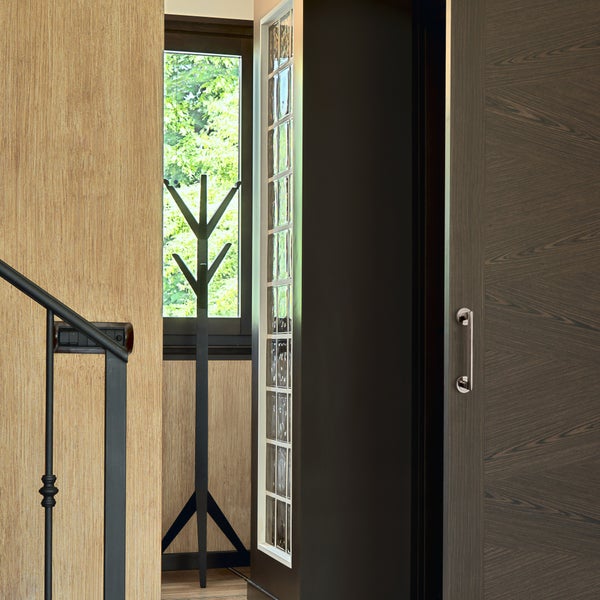 Moderne Innentür mit Schiebesystem, Holzoptik, angrenzend ein Glasbausteinelement und eine Garderobe vor einem Fenster mit Gartenblick.