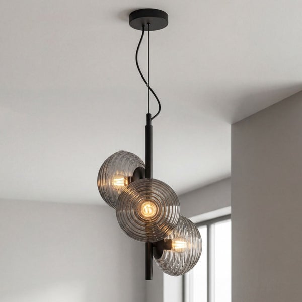 Moderne dreiflammige Pendelleuchte mit schwarzem Metallgestell und geriffelten Rauchglas-Schirmen in einem hellen, minimalistischen Raum.