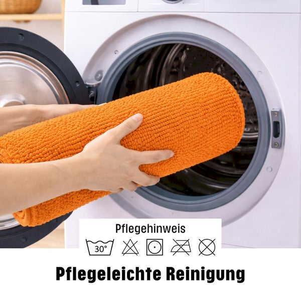 Eine gerollte strukturierte Badematte wird in eine Waschmaschine gelegt mit Pflegehinweisen für die Reinigung bei 30 Grad.