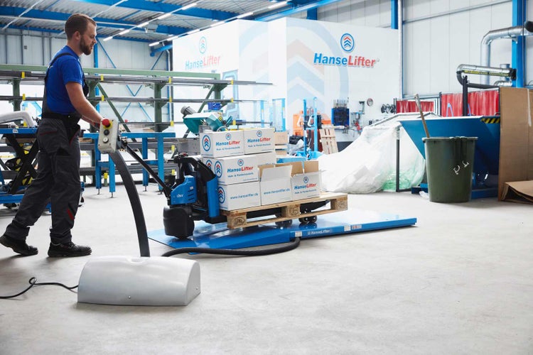 Ein Mitarbeiter bedient einen elektrischen Hubwagen auf einer Bodenwaage in einer Industriehalle mit HanseLifter Firmenlogo.