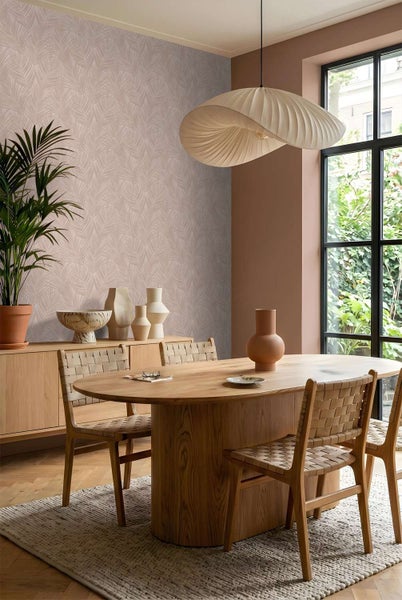 Esszimmer mit Tapete mit Blattmuster, Holzmöbeln, geflochtenen Stühlen und einer Pendelleuchte vor einem großen Fenster mit Gartenblick.