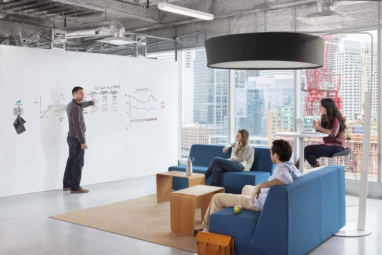 Modernes Büro mit großem Whiteboard, blauen Polstermöbeln und einer großen runden Pendelleuchte in heller Atmosphäre.