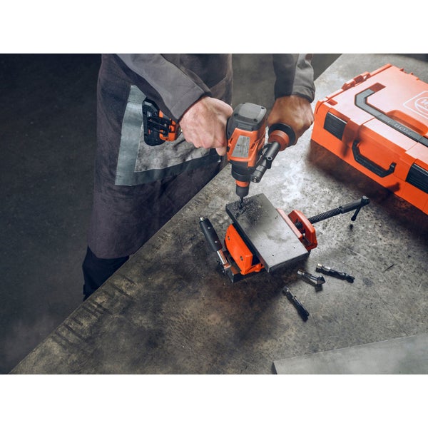 Akku-Bohrmaschine bohrt Loch in Werkstück, befestigt mit Schraubstock; Bohrer liegen bereit