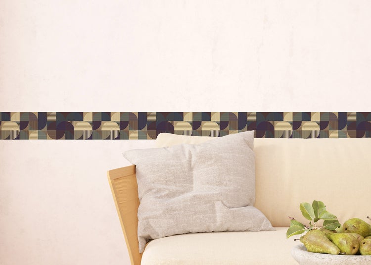 Selbstklebende Tapetenbordüre mit geometrischem Art-déco-Muster an einer Wand in einem modernen, hellen Wohnzimmer mit Sessel und Beistelltisch.