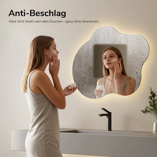 Asymmetrischer Badspiegel mit Beleuchtung und Anti-Beschlag-Funktion, Frau trägt Gesichtscreme auf, klares Sichtfeld trotz Feuchtigkeit.