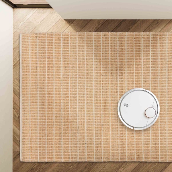 Rechteckiger gewebter Teppich mit beigem Blockmuster auf Holzboden und einem Saugroboter.