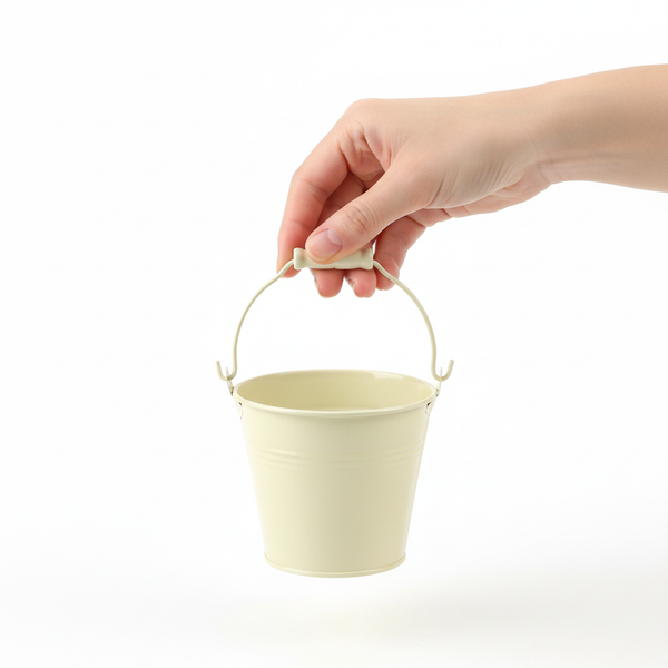 Eine Hand hält einen kleinen beigen Dekoeimer aus Metall am Henkel.