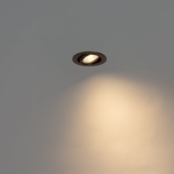 Schwenkbarer Einbaustrahler in dunkler runder Optik an der Decke mit warmweißem Lichtstrahl.