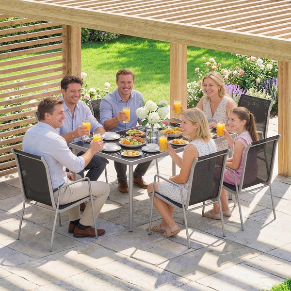 Gruppe beim Essen an einem Gartentisch mit Gartenstühlen unter einer Holzpergola auf einer Steinterrasse.