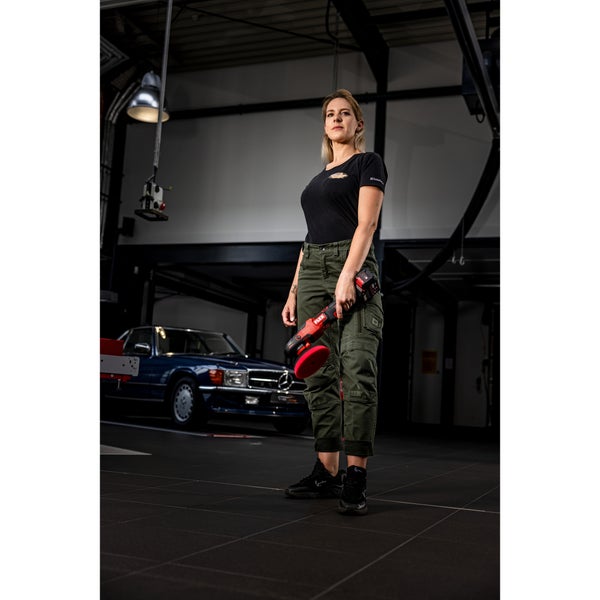 Eine Frau hält eine kabellose Poliermaschine von Flex in einer Werkstatt mit einem klassischen Fahrzeug im Hintergrund.