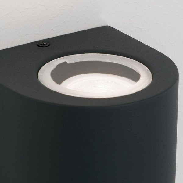 Schwarze Außenwandleuchte aus Metall mit rundem Glaseinsatz und sichtbarem Leuchtmittel.