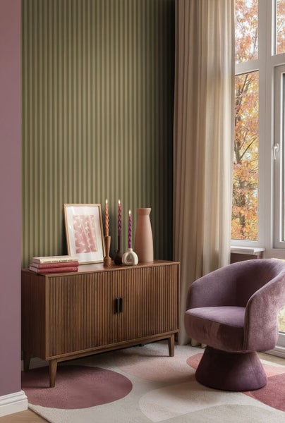 Wohnraum mit Holzkommode, Dekoration und Sessel auf einem gemusterten Teppich