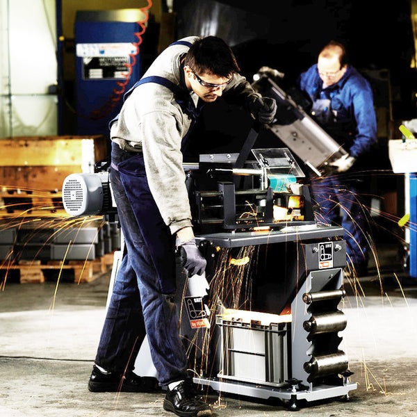 Ein Arbeiter bedient ein stationäres Rohrausschleifgerät in einer Werkstatt, während beim Schleifen von Metall Funken sprühen.