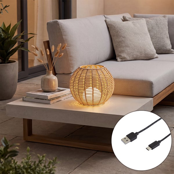Dekorative Tischleuchte aus Rattan auf einem Betontisch neben einem Sofa im Außenbereich mit USB Ladekabel