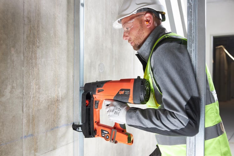 Handwerker mit Schutzausrüstung nutzt ein Bolzensetzgerät an einer Betonwand für die Montage einer Metallständerwand.