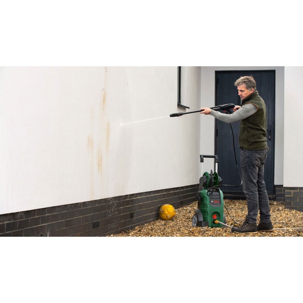 Ein Mann reinigt eine verschmutzte Hauswand mit einem Bosch Hochdruckreiniger auf einer Kiesfläche.