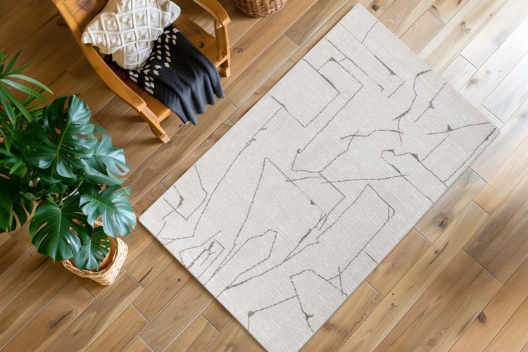 Wohnzimmer mit einem modernen Teppich mit abstraktem Linienmuster auf einem Holzboden, daneben ein Sessel mit Decke und eine Zimmerpflanze.