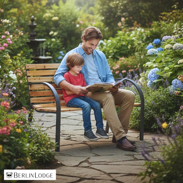 Mann und Kind lesen auf einer Gartenbank aus Holz und Metall in einem hellen blühenden Garten mit Steinweg und Springbrunnen. BerlinLodge Logo.