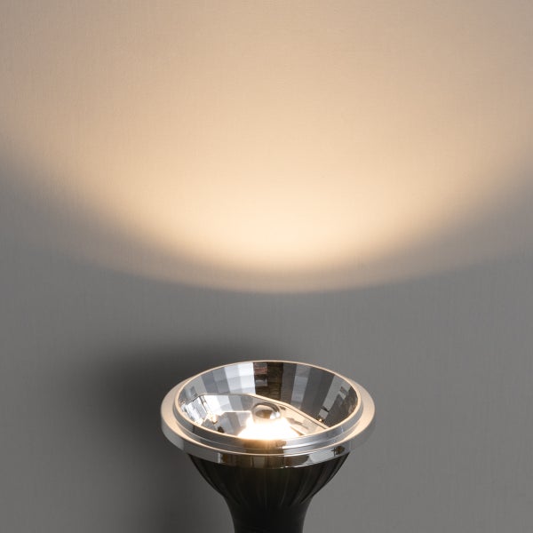 Eingeschaltete Reflektorlampe mit facettiertem Reflektor und warmweißem Lichtkegel an einer Wand.