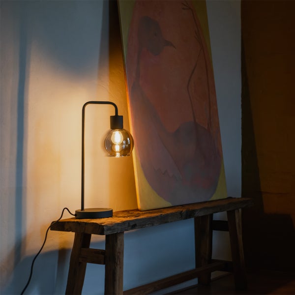 Dekorative Tischleuchte mit Kugelglas auf einer Holzbank neben einem Gemälde