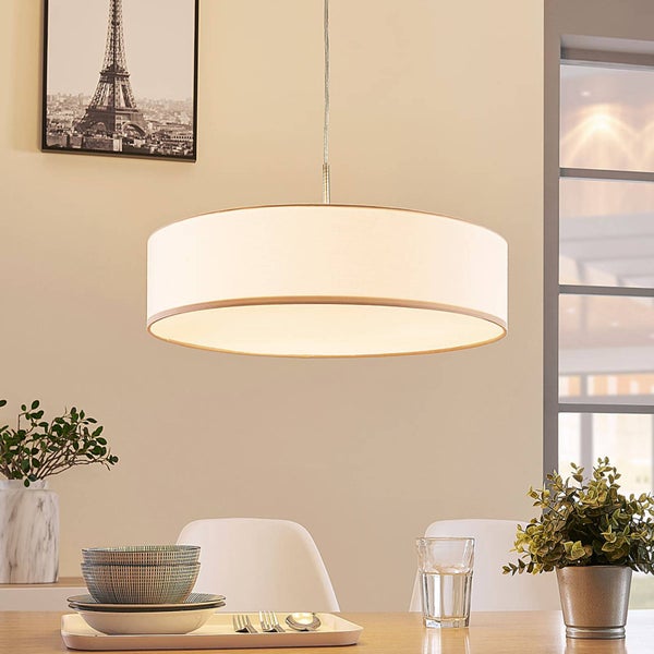 Moderne Pendelleuchte mit rundem Textilschirm in einem hellen, organisierten Esszimmer über einem Holztisch mit Geschirr und Pflanzen.