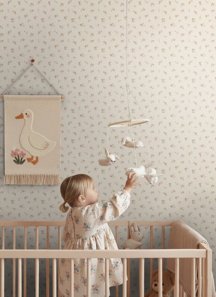 Vliestapete mit floralem Muster in einem Kinderzimmer mit Holzgitterbett, Wandbehang und Mobile.